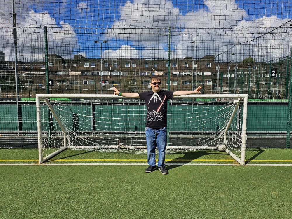 A person stands at a football goal with arms outstretched ready to save a goal.