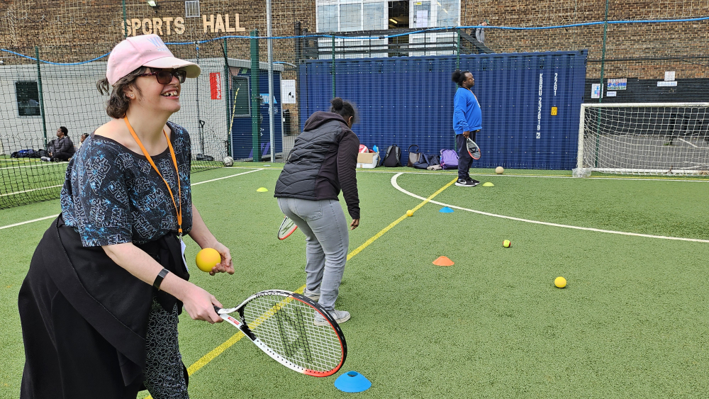 A lady stands with a tennis racket waiting to hit the ball