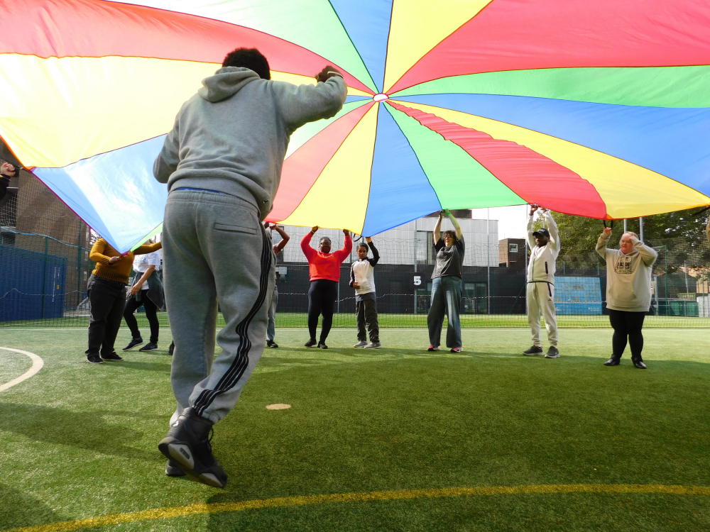 A person runs under a colourful parachute that other people are holding and swirling in the air.