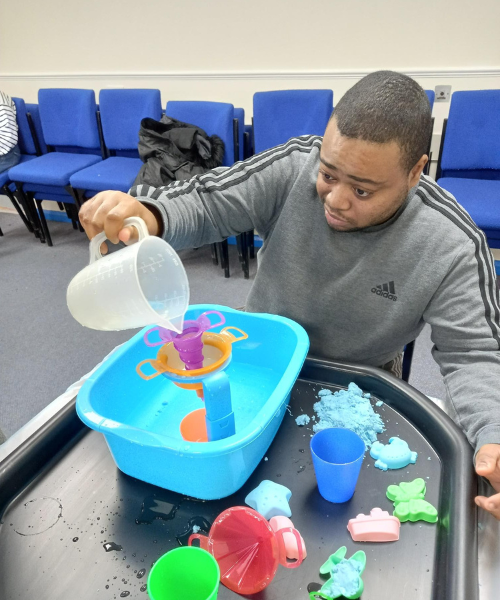 A man pours water from a jug into a plastic basin, as part of sensory exploration