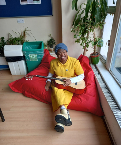 A lady sits on a large red beanbag playing guitar