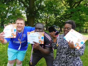 Group of Share adult students stand with arms around each other holding up certificates