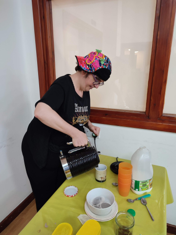 A lady makes a cup of tea, pouring water from a kettle.