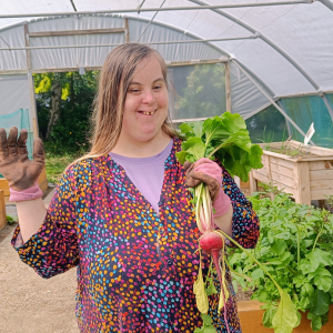 A lady stands in a polytunnel holding up a freshly harvested radish