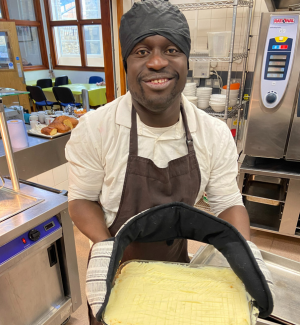 A man stands in a professional kitchen holding a shepherd's pie that's about to go into the oven