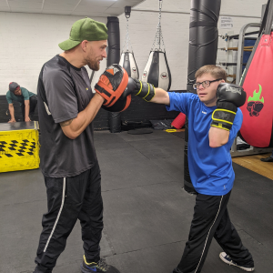 A man stands sparring with a boxing partner in a boxing gym.