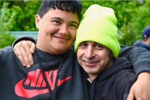 Two people stand smiling arm in arm in a garden