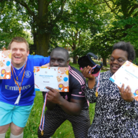 Group of Share adult students stand with arms around each other holding up certificates