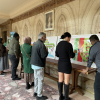 A line of people stand looking at the artworks on display