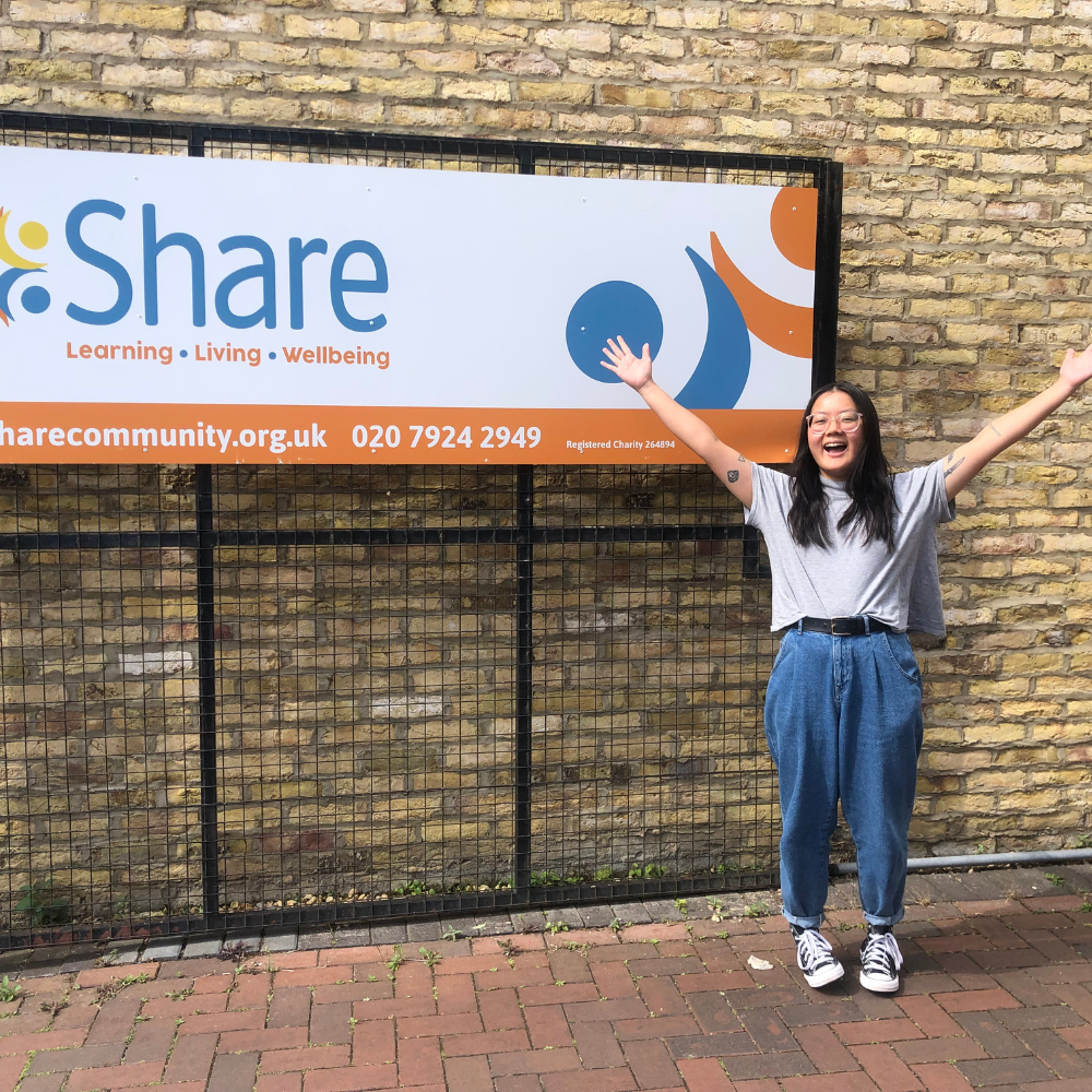 A lady stands with her hands in the air outside Share's main building sign