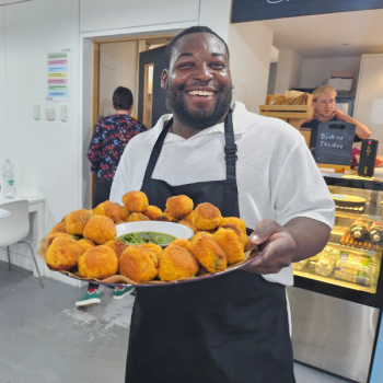 A man stands smiling and holding a serving platter of food