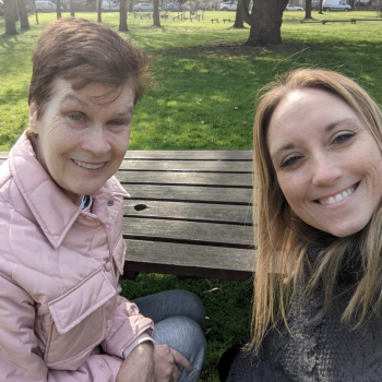 Two ladies take a selfie on a park bench.