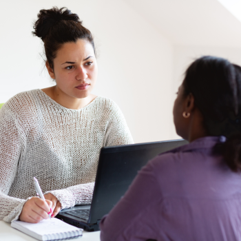 A lady sits at a desk listening to a client and writing notes