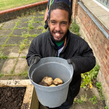 A man is outside holding up a bucket of newly harvested potatoes