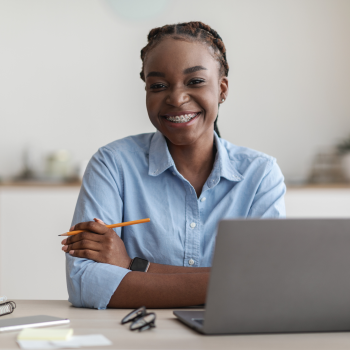 A lady sits smiling at a desk with a computer