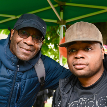 A man and his son stand under a garden umbrella looking at the camera