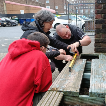 Share students measure wood for a planter with their tutor