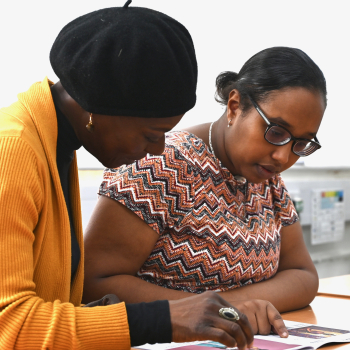 A teacher helps a student with their work sitting at a desk.