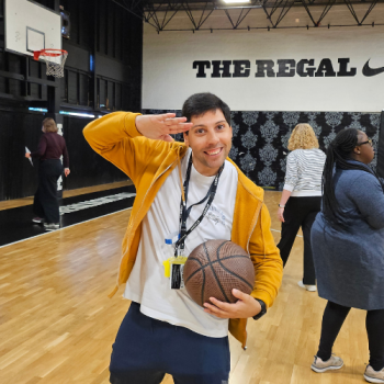 A man stands and salutes on a basketball court while he's holding a basketball about to play.