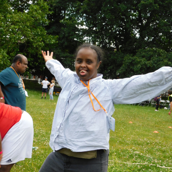 A lady stands in a park smiling at the camera and giving a thumbs up