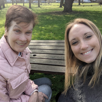 Two women sit on a park bench smiling at the camera for a selfie