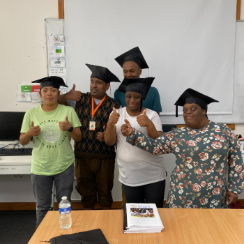 A group of Share students stand with mortar boards on their heads giving a thumbs up at graduation.